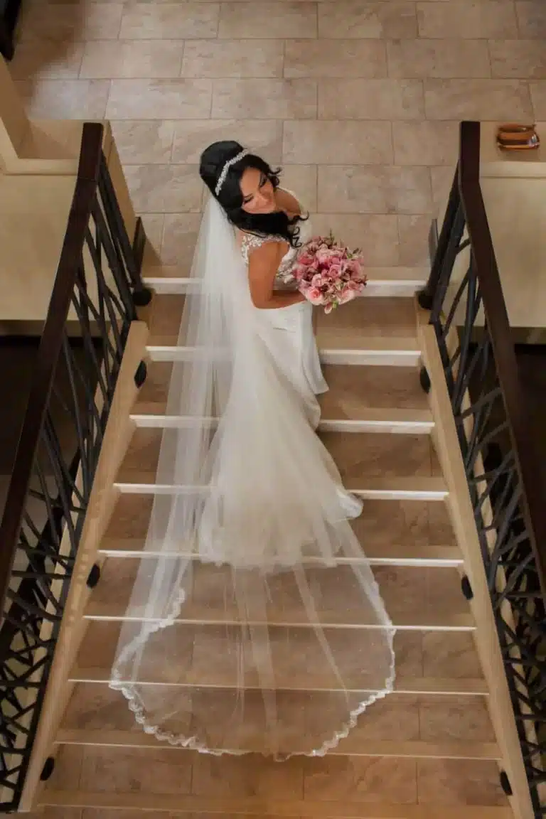 Costa Rica wedding venue bride walking down a grand staircase at a luxury villa, holding a bouquet and wearing a long veil and gown