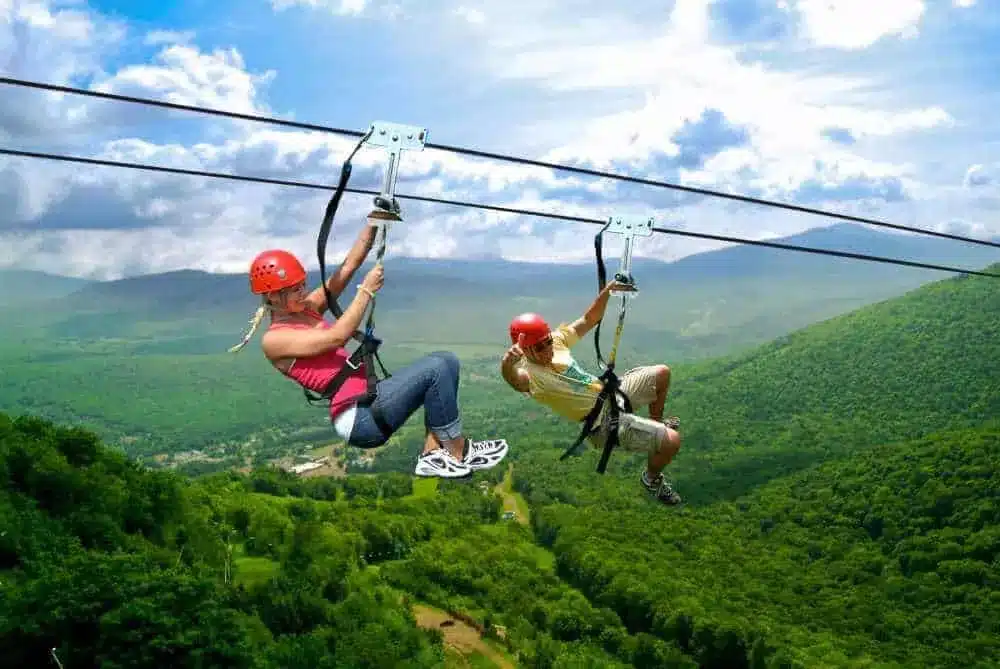 Two travelers zip-lining through Costa Rica’s vibrant rainforest on an adventure tour with sweeping mountain views in Manuel Antonio