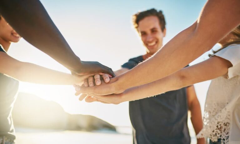 A huddle of people at a corporate bonding event on the beach with hands in as a team.
