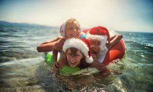 A picture depicting children in Christmas hats playing in the ocean.