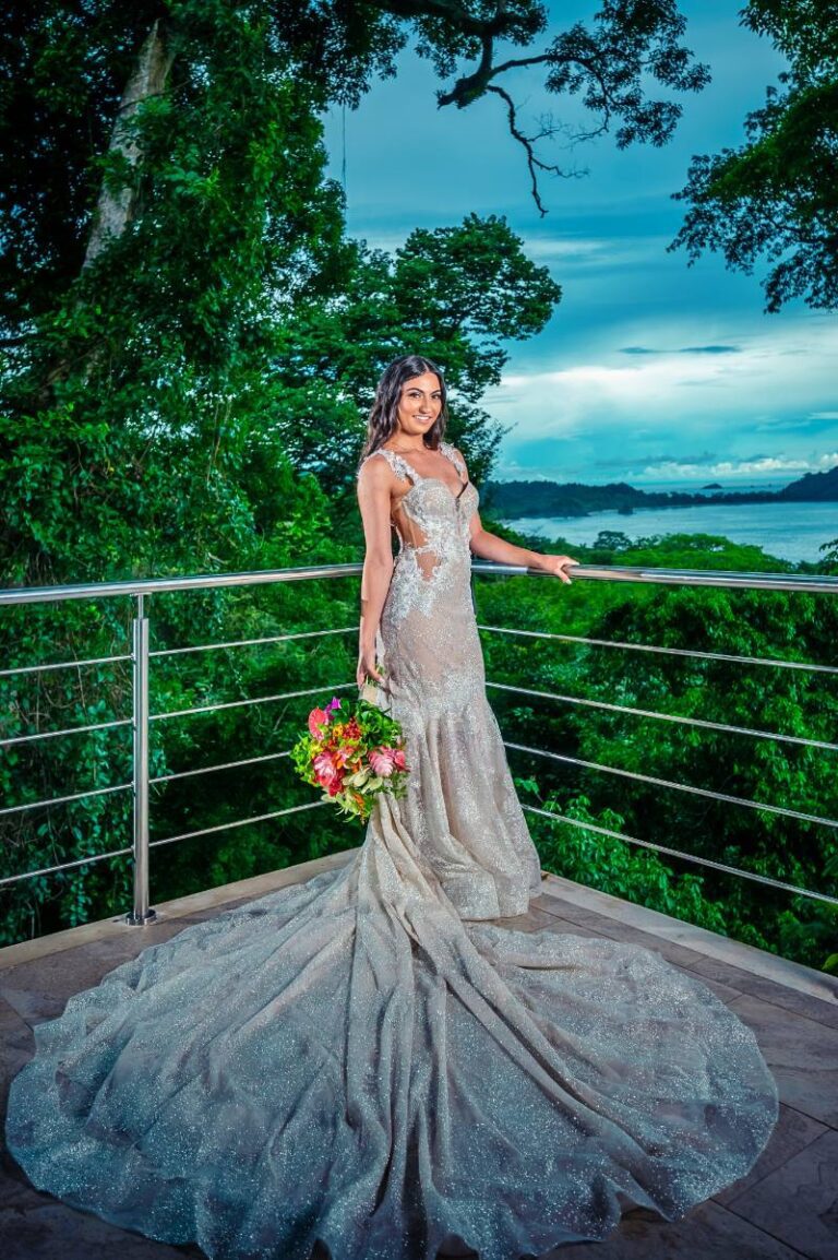 Costa Rica destination wedding bride in sparkling gown holding flowers on a scenic balcony with ocean views at the wedding venue
