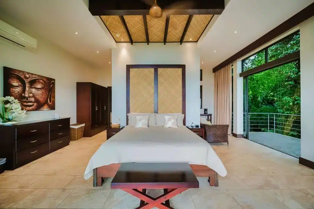 Elegant luxury bedroom in Costa Rica featuring a king bed, modern décor, natural wood accents, and floor-to-ceiling windows overlooking lush rainforest